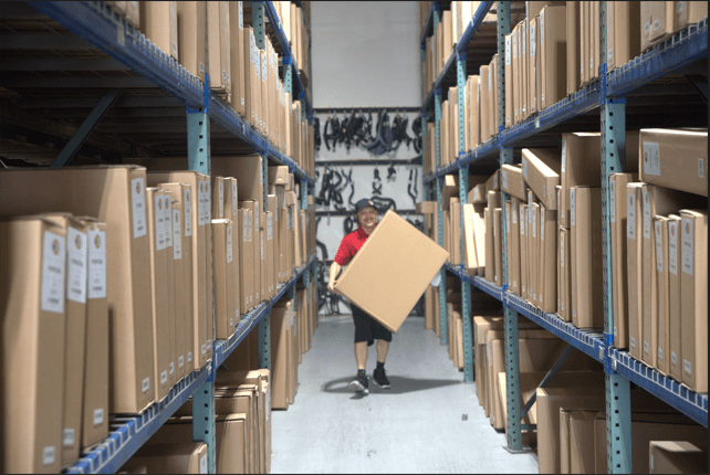 Warehouse interior with lots of parts in boxes on shelves and a guy holding a box.